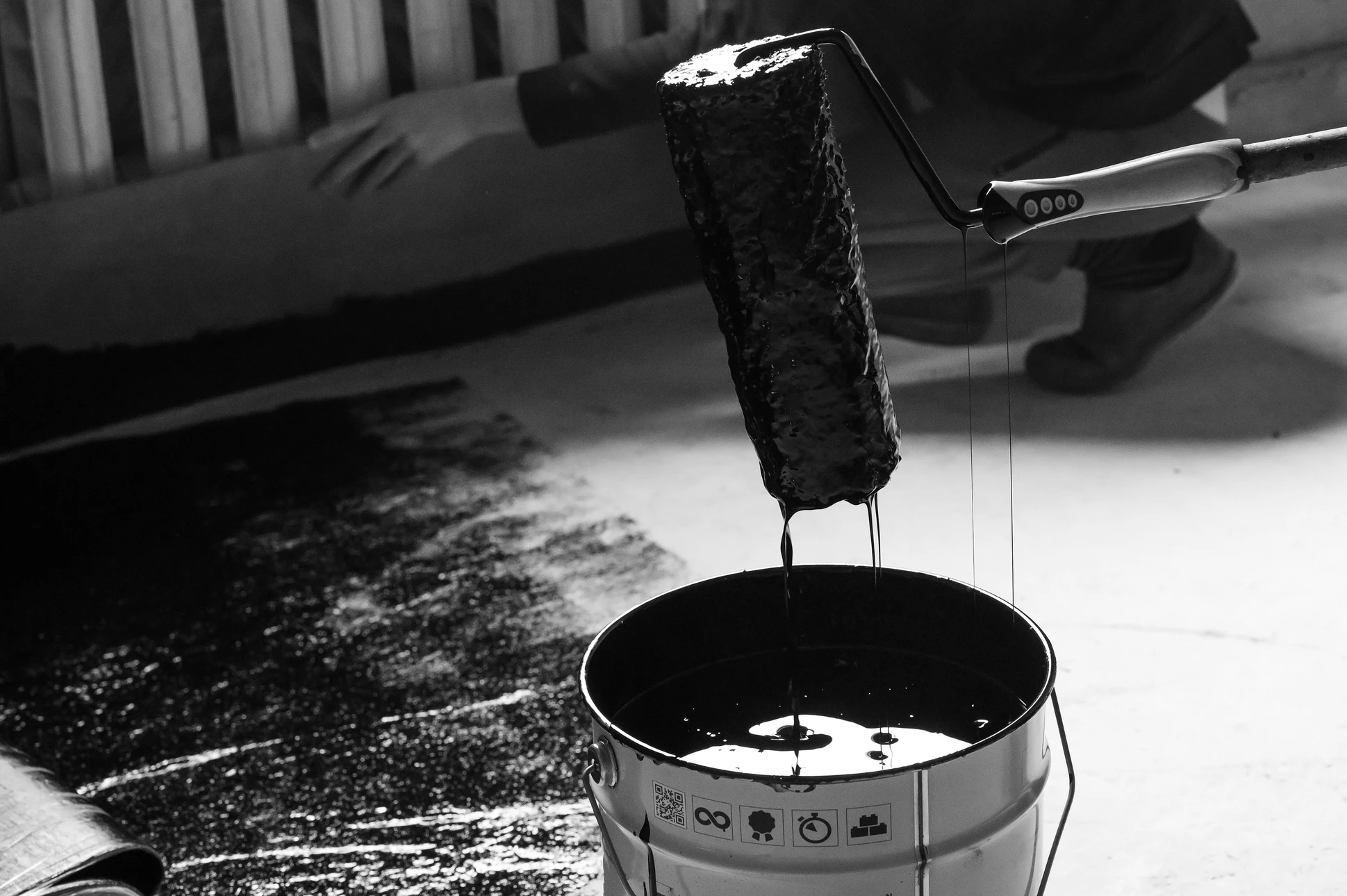 Scène d'étanchéité en extérieur avec application de bitume liquide coulant d'un conteneur textile vers un seau métallique gradué