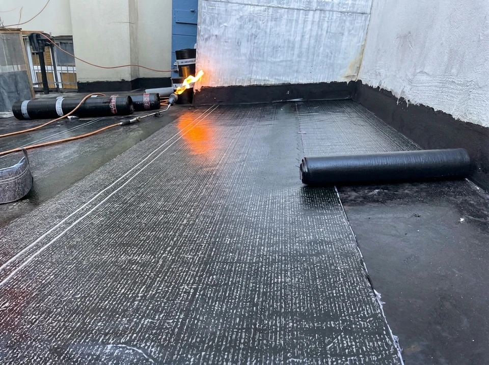 Chantier extérieur de revêtement de sol où un ouvrier applique un enduit de protection liquide bleu sur une surface bétonnée