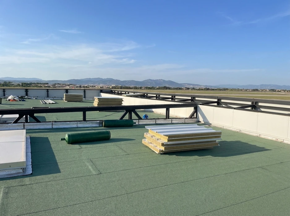 Chantier de construction extérieur avec ouvrier déroulant membrane d'étanchéité bitumineuse sur toiture-terrasse